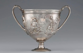 Copa de plata con dos asas, pie, y relieves que muestran figuras humanas y elementos de paisaje