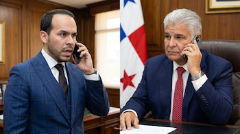 Dos hombres con traje, uno de cuadros azul y otro azul marino, hablan por teléfono. Al fondo se ve la bandera de Panamá.