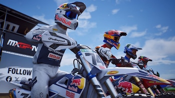 Varios motociclistas con cascos, gafas y trajes de competición se encuentran alineados sobre sus motocicletas bajo un cielo despejado