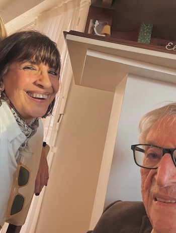 Primer plano de la actriz Cecilia Roth sonriendo, con cabello oscuro y flequillo, junto a un hombre con gafas y bigote. Ella sostiene unas gafas de sol