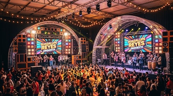 Personas bailando frente a dos escenarios con luces y pantallas con el texto Guadalupe Reyes Orquesta.