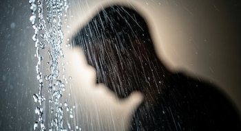 Gotas de agua visibles en primer plano con una silueta borrosa de la cabeza y parte del hombro de una persona al fondo.