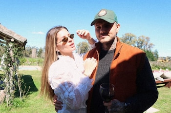 Un hombre con gorra verde y chaleco naranja sostiene una copa junto a una mujer con gafas de sol y blusa blanca