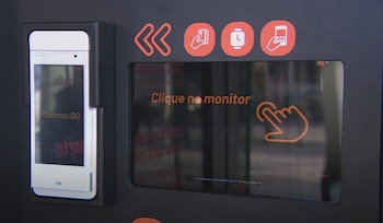 Teléfono inteligente blanco en soporte y pantalla táctil negra con texto en portugués 'Clique no monitor', un icono de mano y símbolos de pago y reloj
