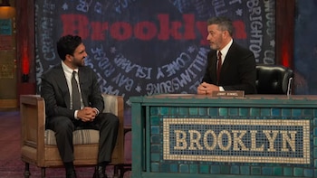 Jimmy Kimmel sentado tras un escritorio con su nombre junto a un hombre en traje en un sillón, frente a un fondo con la palabra Brooklyn