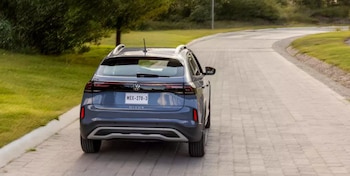 Vista trasera de un automóvil Volkswagen Nivus SUV azul oscuro en un camino de adoquines con pasto y árboles. Placa de México MEX-270-3