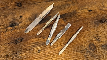 Cinco pinzas metálicas de distintos tamaños dispuestas sobre una tabla de madera oscura con vetas.