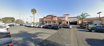 Exterior de El Super en Walnut Park, con un edificio de tonos claros, un estacionamiento con numerosos coches y una palmera bajo cielo azul