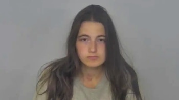 Una mujer con cabello oscuro largo y una camiseta clara posa de frente en una fotografía policial con un fondo gris claro