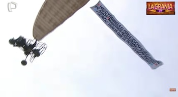 Vista aérea de una avioneta blanca remolcando una pancarta larga con texto negro sobre el cielo despejado, con logos de televisión