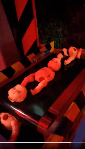 Varias cabezas y cuerpos de muñecos de plástico sobre una cinta transportadora negra en un entorno con iluminación roja