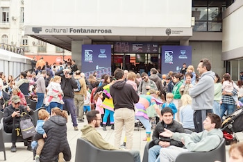 Multitud de personas en una plaza seca frente a la entrada de un edificio con carteles de FILROS y la inscripción cultural Fontanarrosa