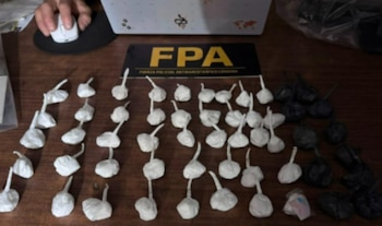 Una mano manipula un ratón de computadora, junto a varios paquetes pequeños blancos y negros, y un cartel de la FPA sobre una mesa de madera
