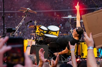 Lars Ulrich, baterista con gorra negra y camiseta, recostado sobre su batería amarilla con un brazo levantado, frente a una multitud