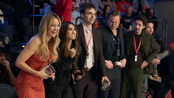 Kate Hudson sonriendo en vestido rojo, Mindy Kaling con expresión intensa, y Drew Tarver observando entre un grupo de personas en un evento