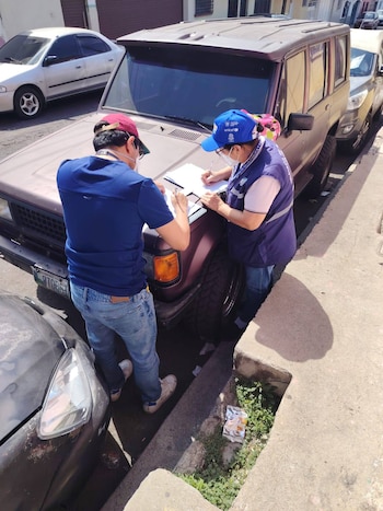 Una trabajadora de la salud con mascarilla y uniforme azul inyecta una vacuna en el brazo de una persona en un espacio interior