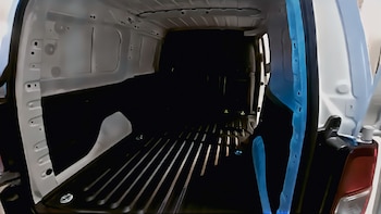 Interior vacío de la zona de carga de una furgoneta blanca, con el suelo oscuro y estriado, paredes claras y detalles en azul a los lados de la puerta trasera