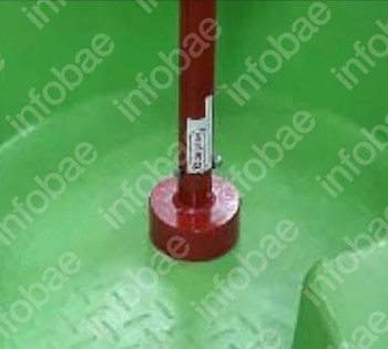Pilar metálico rojo vertical con una abrazadera, anclado a una base metálica redonda roja sobre una superficie de color verde claro