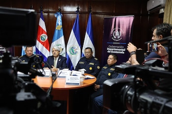 Varios hombres, incluyendo oficiales de policía y un funcionario en traje, sentados en una mesa con banderas de Costa Rica, El Salvador, Honduras y Guatemala de fondo