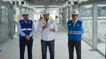 Tres hombres con cascos de seguridad y chalecos institucionales permanecen en el interior de una estación de autobús cubierta de vidrio