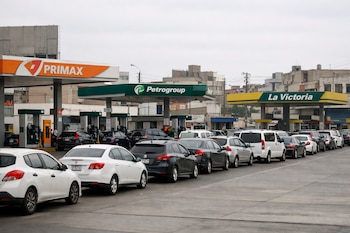 Una estación de servicio en Lima con largas filas de autos. Se observan surtidores de combustible y marquesinas con logos de Primax, Petrogroup y La Victoria. Edificios urbanos al fondo.