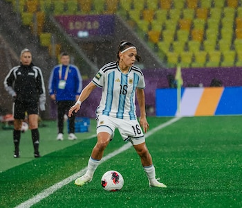 Una jugadora con el uniforme albiceleste número 16 conduce un balón sobre una cancha de fútbol mojada