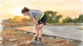 Una mujer con ropa deportiva está inclinada con las manos en las rodillas en un camino al aire libre con árboles al atardecer.
