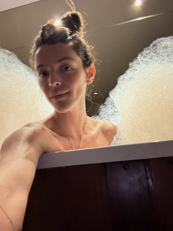 Selfie de Calu Rivero en una bañera con burbujas. Se ve su torso desnudo, su cabello recogido en un moño y un collar delgado