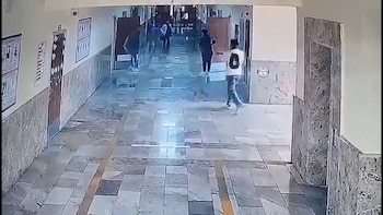 Vista aérea de un pasillo interior con personas caminando, paredes claras y piso de baldosas gris y beige con franjas amarillas