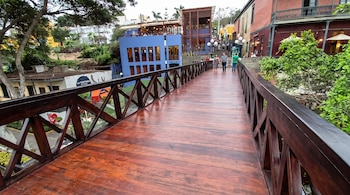 Un puente de madera recién restaurado sobre el cual caminan varias personas, rodeado de edificios coloridos y vegetación