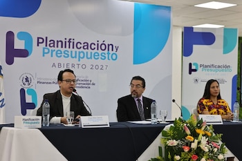 Tres panelistas, dos hombres y una mujer, sentados en una mesa con micrófonos durante una sesión. Detrás, se ven banners con "Planificación y Presupuesto Abierto 2027"