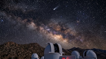 Cúpulas blancas de un observatorio astronómico bajo un cielo nocturno estrellado con la Vía Láctea y un cometa.