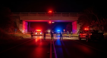 Noche en carretera federal. Puente de concreto, luces policiales rojas y azules. Agentes de uniforme oscuro, chalecos tácticos, cinta amarilla. Camioneta Guardia Nacional.