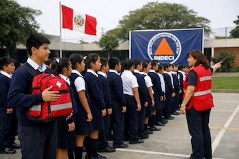 Grupo de estudiantes con uniformes escolares formados en filas durante un simulacro, una docente los guía, al fondo bandera peruana y pancarta de INDECI.