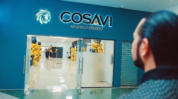 Entrada a un establecimiento COSAVI Ahorro y Crédito con puertas de vidrio y columnas de globos dorados y negros; un hombre de espaldas en primer plano.