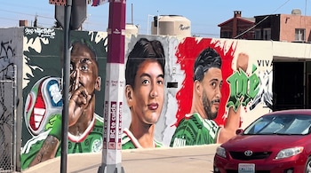 Cena de rua com três figuras de homens, um com uma bola e uma camiseta verde e vermelha. Inclui texto, carros vermelhos, cercas e edifícios.