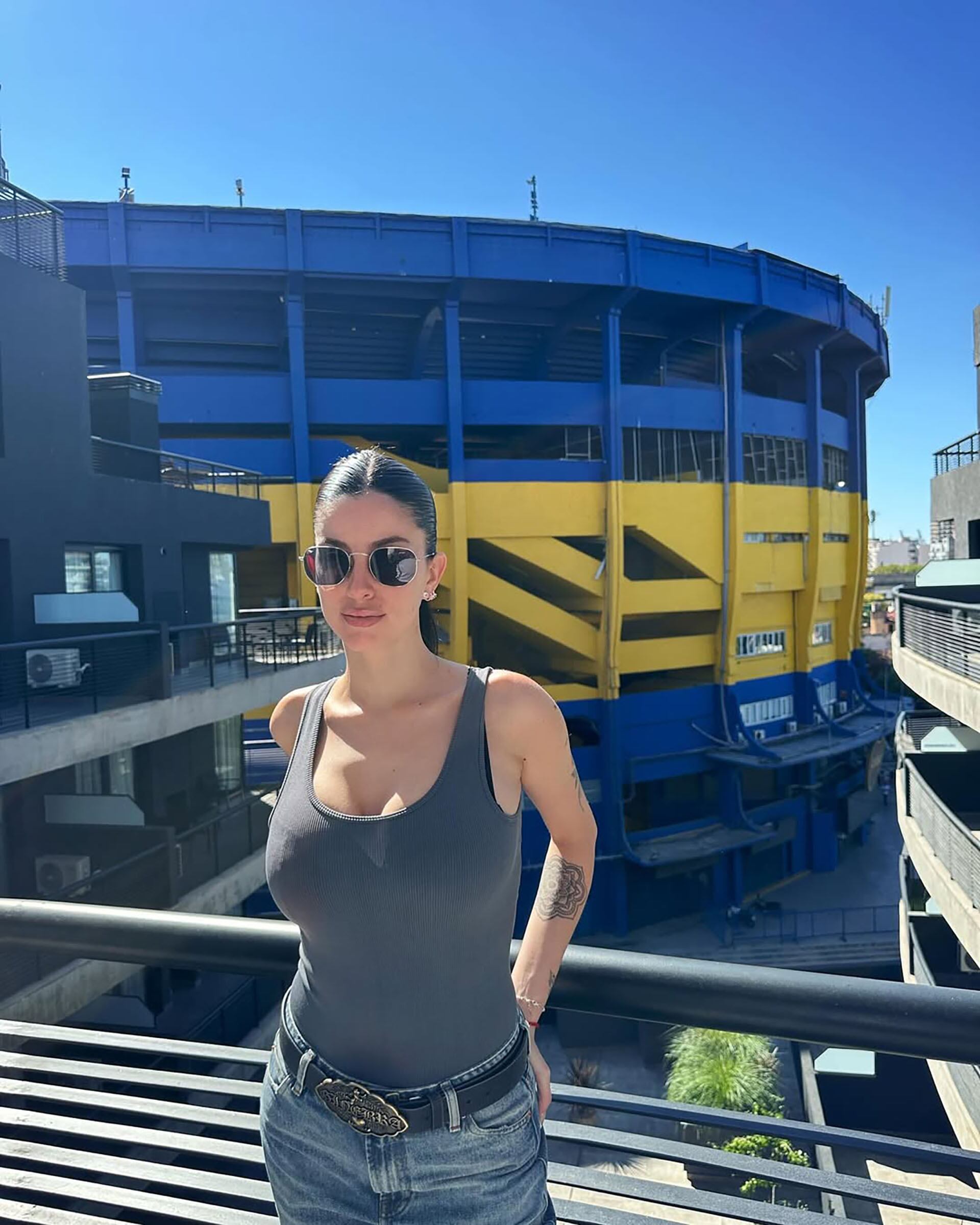 La joven fanática de Boca Juniors que se hizo viral posa sonriente desde un balcón con el icónico estadio La Bombonera de fondo, en un día soleado.