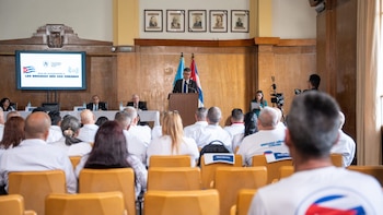 Un hombre habla en un podio con banderas de Cuba y Costa Rica, ante una pantalla, funcionarios y una audiencia en un salón