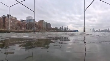 Imagen tomada desde el agua mostrando edificios y la orilla de una ciudad bajo un cielo nublado, con rascacielos y torres a lo lejos