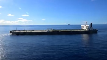 Un gran buque petrolero de color oscuro con la superestructura blanca navega hacia la derecha en aguas azules bajo un cielo despejado