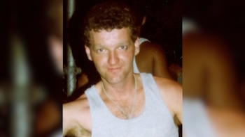 Primer plano de un hombre caucásico de mediana edad con cabello castaño rizado y una camiseta sin mangas gris, mirando directamente a la cámara