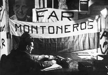 Fotografía en blanco y negro de un hombre de perfil sentado en un escritorio. Detrás, un cartel que dice 'FAR MONTONEROS' y un retrato de Juan Domingo Perón