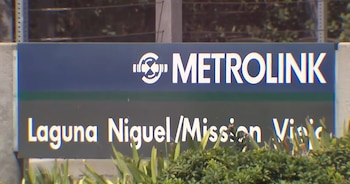 Un cartel azul y gris con el logo blanco de Metrolink y el texto Laguna Niguel/Mission Viejo. En la parte inferior, vegetación verde