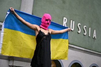 Una integrante del grupo activista Pussy Riot sostiene una bandera ucraniana durante una protesta contra la participación de Rusia (Photo by Marco BERTORELLO / AFP)