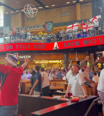 Vista interior de un bar abarrotado de gente, muchos con camisetas de Inglaterra y banderas, observando pantallas y celebrando un evento deportivo en Sagra