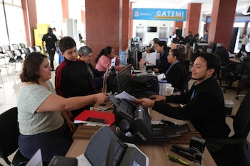 Mujer, niño, empleados, escritorios, computadoras, escáner, papeles, sillas y un cartel azul con la inscripción CATEMI en una oficina