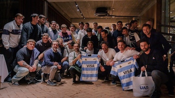 Grupo de treinta hombres posa, algunos arrodillados sostienen dos camisetas de rugby firmadas con logos VISA y Puma, y un bolso UAR