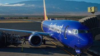 Un avión azul de Southwest Airlines, modelo Boeing 737 Next Generation, está estacionado en una pista con un puente de embarque y un camión de combustible