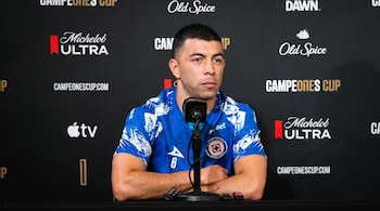 Un hombre con camiseta deportiva azul del equipo Cruz Azul sentado frente a un micrófono en una sala de prensa.