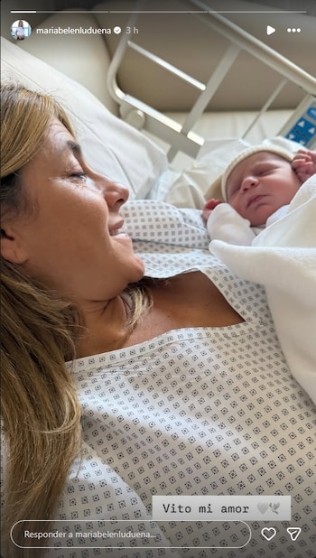 María Belén Ludueña, recostada en una cama de hospital, sonríe mientras mira a su lado a un bebé dormido envuelto en mantas blancas y con un gorrito